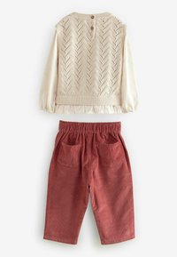 Elfenbenstrikket vest med zigzag mønster og tre knapper bagpå, parret med rustfarvede fløjl bukser med to lommer.