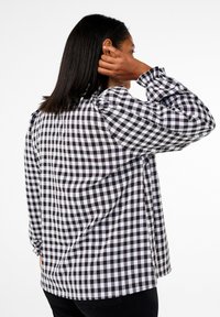 Black and white checked puff-sleeve shirt with a loose fit, featuring elastic cuffs and a round neckline. The fabric appears lightweight.