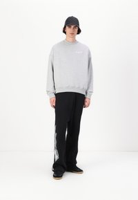 Gray sweatshirt with crew neck, paired with black pants featuring silver flame graphics on the side. Black sneakers complete the outfit.