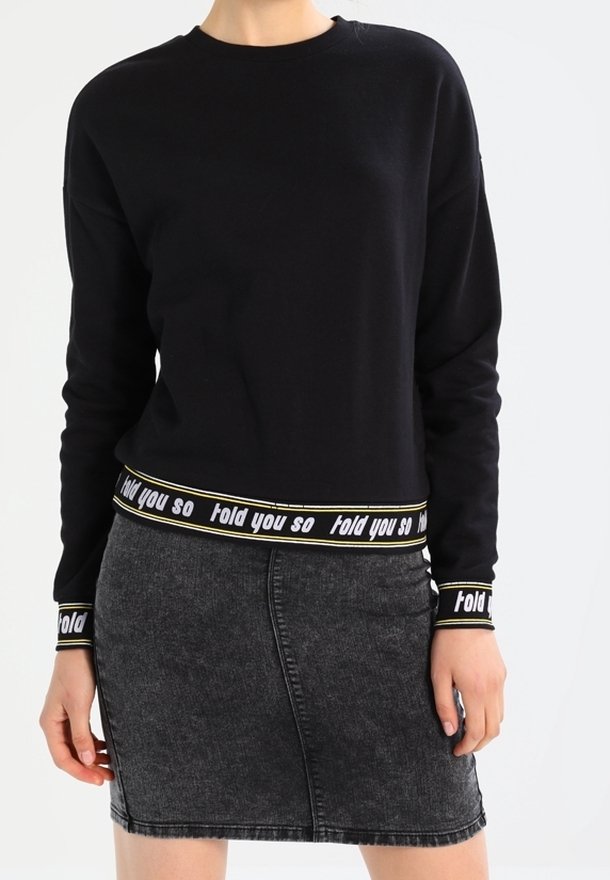 Sudadera negra de manga larga y cuello redondo, con un dobladillo elástico con marca de texto. Combinada con una falda de mezclilla de gris oscuro.