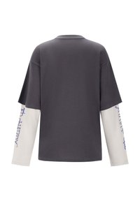 Grijze shirt met korte mouwen en lange witte mouwen. Heeft een bedrukt ontwerp op de witte mouw in blauwe typografie. Standaard pasvorm, gladde textuur.