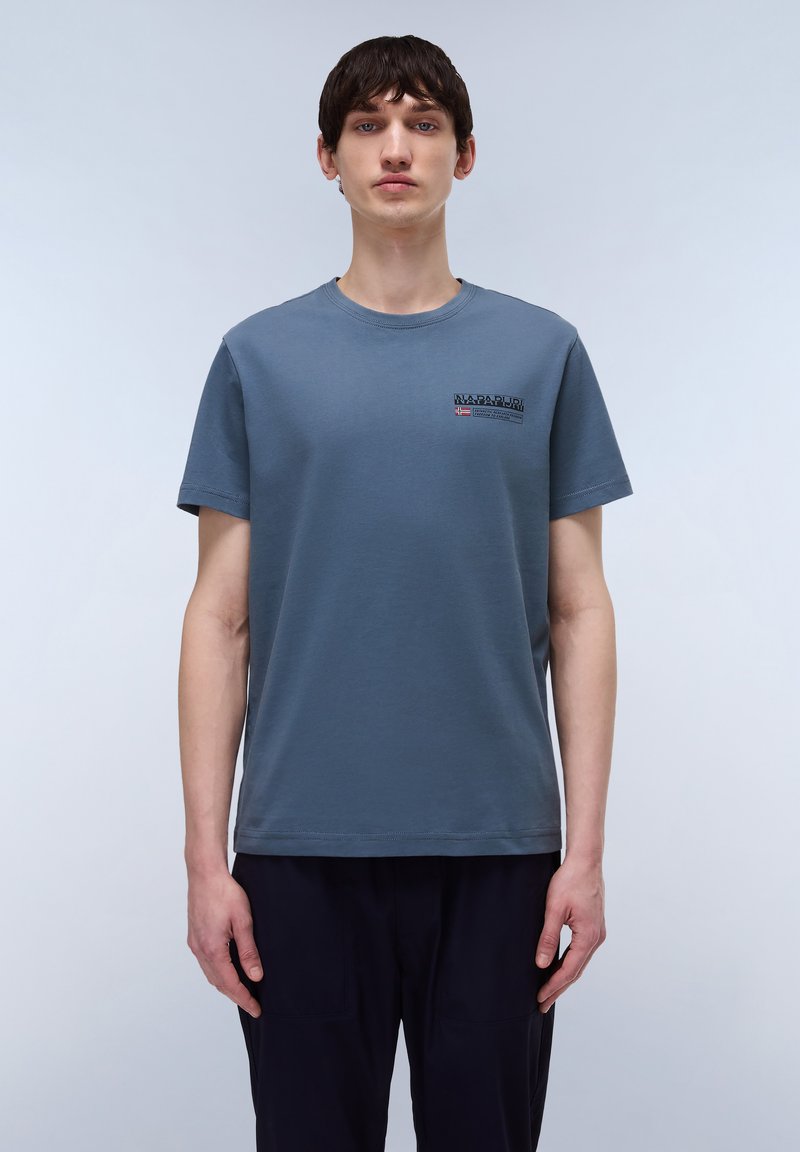 Camiseta de algodón en azul pizarra con mangas cortas, cuello redondo y un pequeño logotipo en negro y rojo. Textura suave, corte relajado.