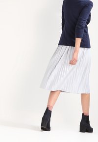 Námořnický dlouhý rukáv spárovaný s plisovanou bílou midi sukni. Outfit doplňují černé kotníkové boty a světle růžové ponožky.