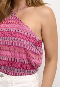 Ärmlös topp med ett rosa och flerfärgat vågmönster. Materialet verkar lätt och har en strukturerad yta. Bärdesignen är korskorsad.