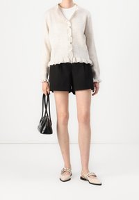 Cárdigan de punto beige claro con un dobladillo con volantes, pantalones cortos negros y bailarinas beige claro con moños. Bolso negro con dos asas.