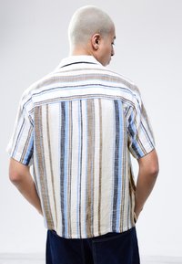 Short-sleeve shirt made of lightweight fabric featuring vertical stripes in beige, brown, and blue, with a relaxed fit and a collar.