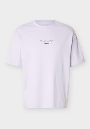 Λευκό κοντομάνικο μπλουζάκι με το κείμενο "Calvin Klein JEANS" τυπωμένο στο κέντρο του στήθους με μαύρα γράμματα.