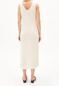 Robe sans manches en tricot couleur blanc cassé avec un décolleté en V et des fentes latérales, présentant une silhouette ajustée et une texture côtelée. Sandales plates incluses.