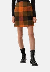 Wollen gemengde geruite rok met oranje, zwarte en bruine vierkanten. A-lijn snit met een gladde textuur, gestyled met zwarte combatboots.