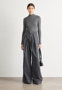 Una blusa gris de manga larga combinada con pantalones de pierna ancha de talle alto en gris oscuro. El conjunto incluye un cinturón con una hebilla de metal y un bolso negro.