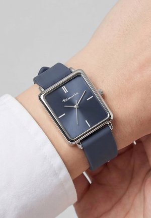 Armbanduhr mit quadratischem silbernem Gehäuse, blauem Zifferblatt, minimalistischen weißen Stundenmarkierungen und blauem Armband, getragen am linken Handgelenk mit weißer Hemdmanschette.