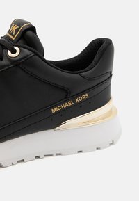 Baskets en cuir noir avec accents dorés, semelle intermédiaire blanche et branding. Comprend un col rembourré et des détails de coutures contrastants.