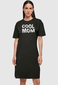 Černé bavlněné šaty ve stylu trička s krátkým rukávem, s nápisem "COOL MOM" v bílé. Jednoduchý kulatý výstřih a délka po kolena.