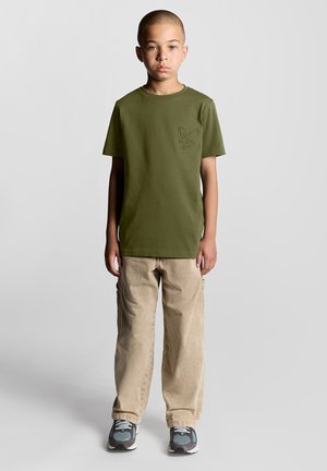 Olijfgroene katoenen T-shirt met korte mouwen, voorzien van een subtiele adelaarsprint. Gecombineerd met beige cargobroeken en sneakers.