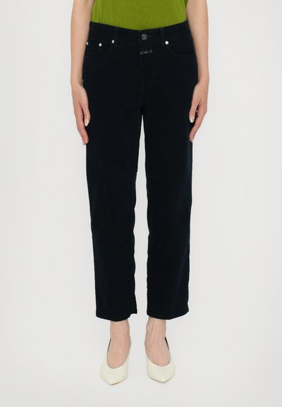 Jeans azul marino con un diseño de pierna recta, que cuentan con cinco bolsillos, cierre de botón en la parte delantera y una textura suave. Combinados con tacones altos blancos.