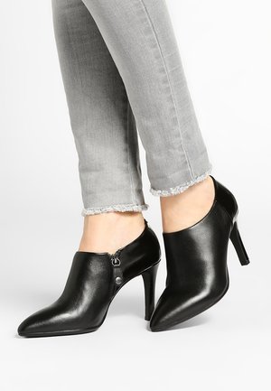 Czarne skórzane szpilki z ostrokątnym noskiem i zamkiem błyskawicznym z boku, w zestawie z przyciętymi szarymi dżinsami o postrzępionych brzegach.