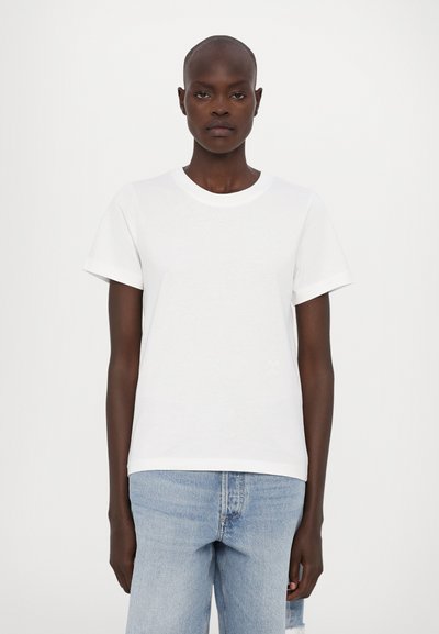 Λευκό βαμβακερό t-shirt με κοντά μανίκια, στρογγυλή λαιμόκοψη και λεία υφή, συνδυασμένο με ανοιχτό μπλε τζιν με σκισίματα.