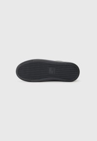 Shoe sole with a textured black rubber surface, featuring a herringbone pattern and subtle branding at the center. Rounded edges.