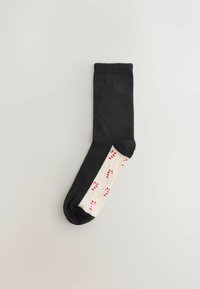 Sort sok med en cremefarvet sektion, der har røde og lyserøde slikstok mønstre. Blødt materiale, standard længde, med manchet i toppen.