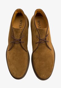 Brązowe zamszowe buty z wiązaniem, okrągłym noskiem i kontrastowymi brązowymi sznurowadłami. Naturalna skórzana podszewka oraz subtelne wytłoczone logo wewnątrz.