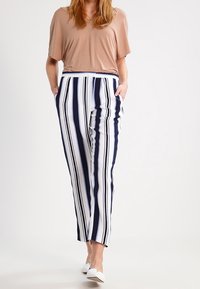 Pruhované kalhoty s námořnickými modrými a bílými svislými pruhy; mají boční kapsy a uvolněný střih. Spárovány s světle hnědým topem a bílými botami.