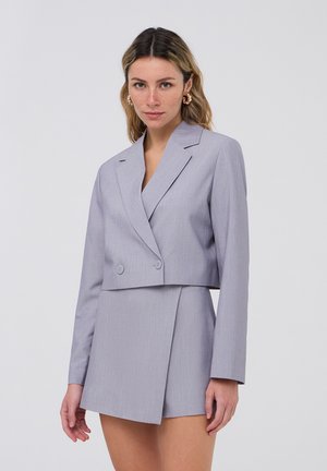 Blazer grigio accorciato con rever a punta, chiusura a doppio bottone e maniche lunghe abbinato a una gonna coordinata con design avvolgente.