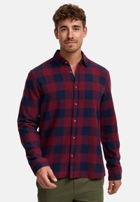 Camisa de franela a cuadros en rojo y azul marino con mangas largas, cierre frontal de botones y botones en contraste. Textura suave con un patrón de cuadros clásico.