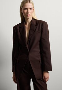 Bruine op maat gemaakte blazer van gladde stof, met een notch-kraag, enkele knoopsluiting en voorkruiszakken.