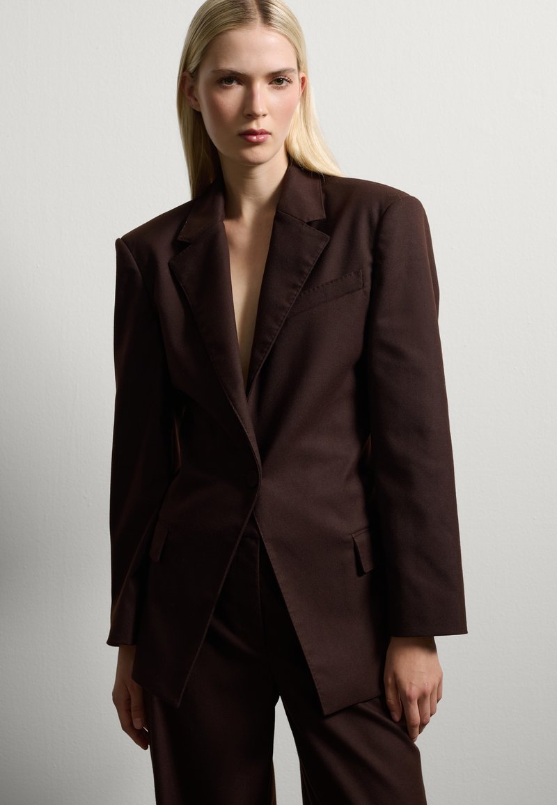 Bruine op maat gemaakte blazer van gladde stof, met een notch-kraag, enkele knoopsluiting en voorkruiszakken.