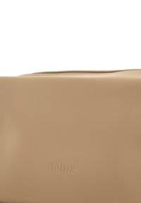 Beige veske laget av glatt, vanntett materiale, med en innfelt glidelås og preget "RAINS"-logo på siden. Rektangulær form.
