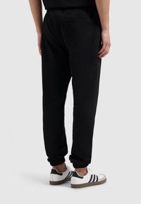 Zwarte joggingsbroek met een elastische tailleband en boorden. Gemaakt van zachte stof, met een achterzak en een ontspannen pasvorm. Gemaakt in combinatie met witte sneakers.