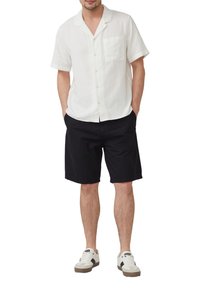 Witte korte mouwen shirt met een zak, gecombineerd met zwarte shorts en witte sneakers met grijze accenten. Casual, lichtgewicht stof.