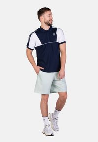 Polo a righe diagonali navy e bianche con maniche corte. Abbinato a pantaloni corti mint chiaro e scarpe da ginnastica.