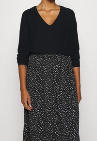 Pull en maille noir avec un col en V et des manches longues, associé à une jupe noire aux motifs abstraits blancs. Texture douce, coupe décontractée.