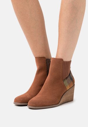 Bottines en daim marron avec un talon compensé, panneau latéral en élastique et accents en textile à carreaux dans des tons terreux. Texture lisse avec un design structuré.