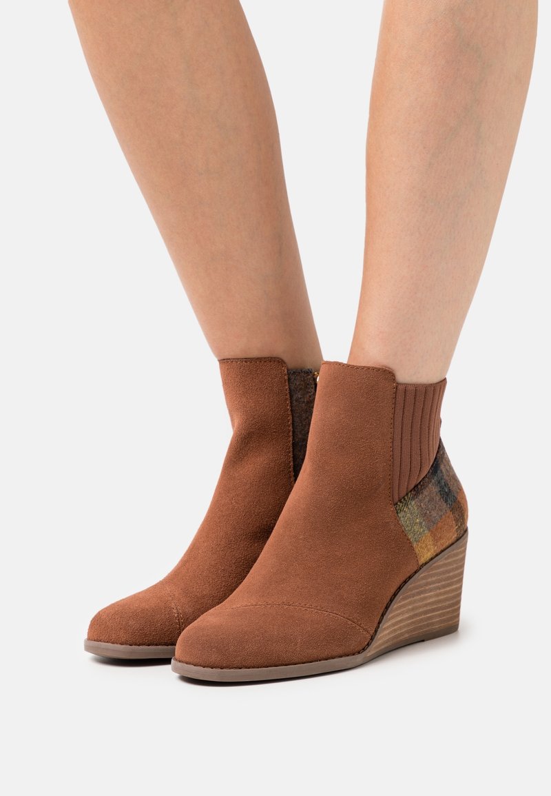 Bottines en daim marron avec un talon compensé, panneau latéral en élastique et accents en textile à carreaux dans des tons terreux. Texture lisse avec un design structuré.
