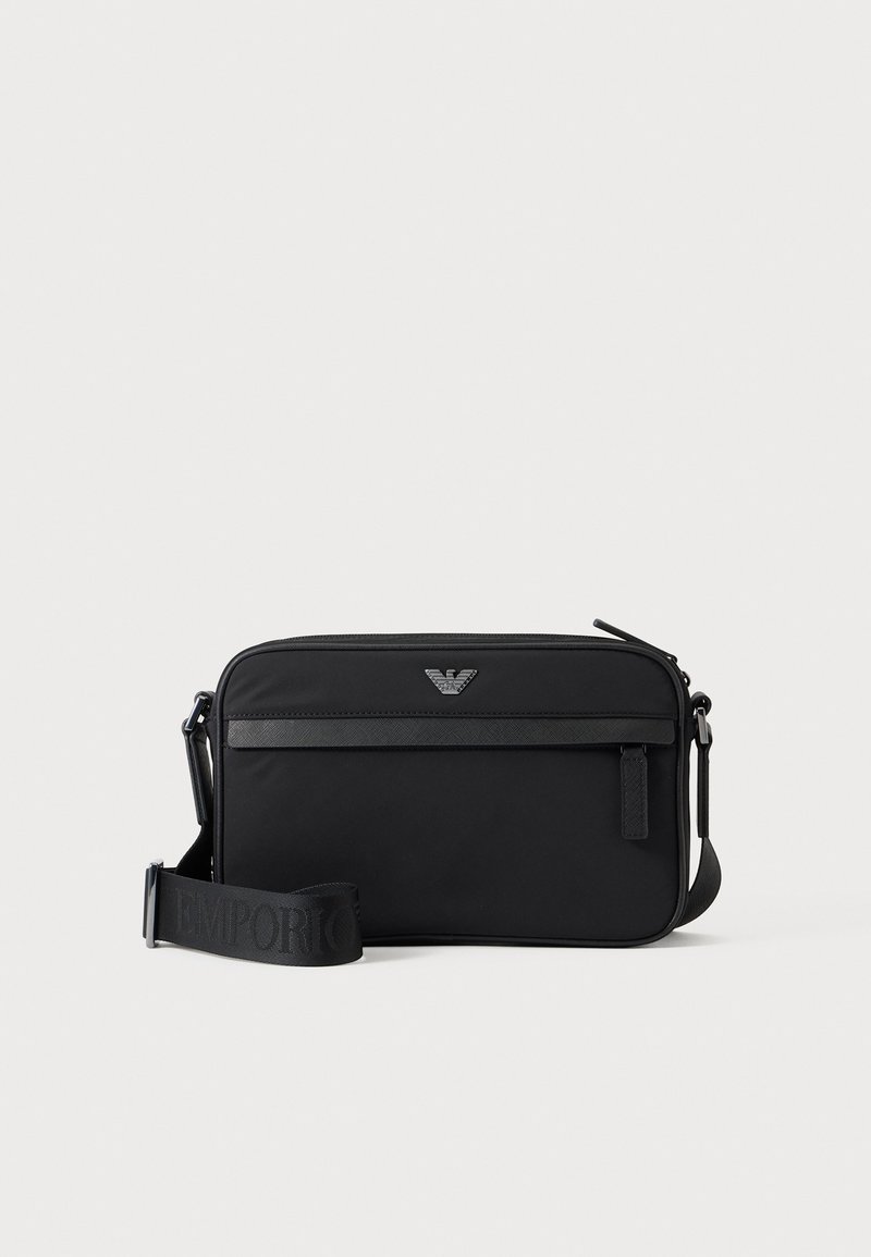 Μαύρη ορθογώνια τσάντα crossbody με μπροστινή τσέπη με φερμουάρ, ρυθμιζόμενο λουρί και μικρό μεταλλικό λογότυπο στο επάνω κέντρο.