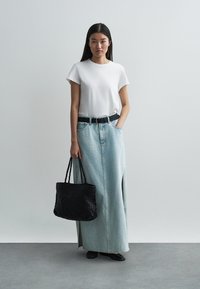 Λευκό βαμβακερό μπλουζάκι, φούστα από ανοιχτό μπλε τζιν μάξι με πλάγιες σχισμές, μαύρη ζώνη μέσης και πλεγμένη μαύρη τσάντα ώμου.