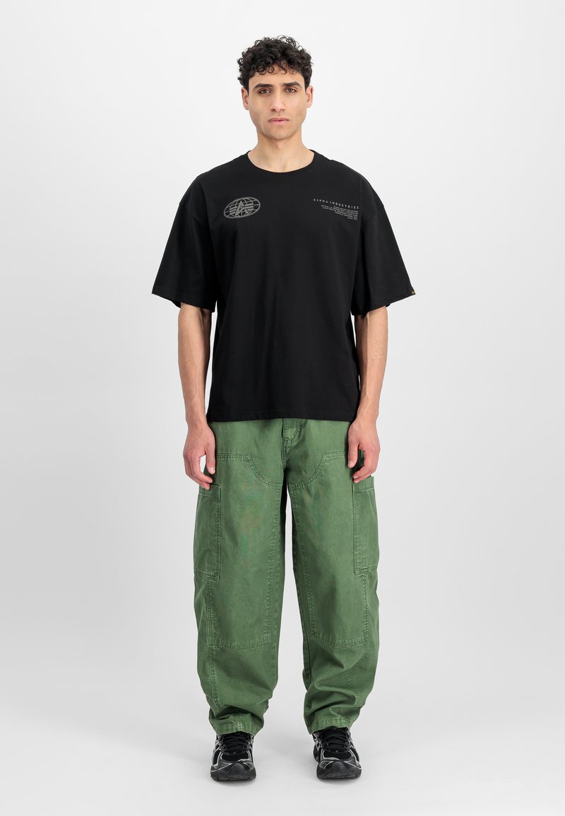 Čierne bavlnené tričko s voľným strihom, krátkymi rukávmi a potlačou loga. Nosí sa s zelenými cargo nohavicami s vreckami a voľným strihom.