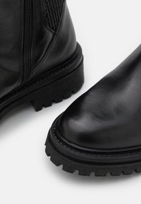 Botas de cuero negro con un acabado suave, suela resistente y detalles de cremallera; los acentos de malla en los lados añaden textura y profundidad.