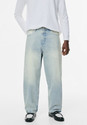 Lichtblauwe, wijde jeans met een vervaagde afwerking en subtiele wassingdetails, gecombineerd met zwarte schoenen en een wit overhemd met lange mouwen.