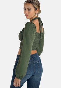 Olivengrøn cropped top med pufærmer og smocket ryg, sat sammen med mørkeblå højttaljede jeans. Toppen har en snøring ved halsen.