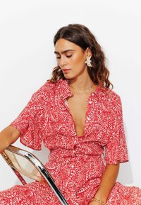 Robe à motifs rouges avec des manches courtes, un décolleté en V profond et une taille cintrée. Présente des motifs paisley complexes et une texture de tissu lisse et fluide.