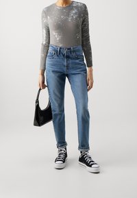 Grey long-sleeve top with a textured pattern, high-waisted blue jeans, black patent handbag, and black high-top sneakers with white soles.