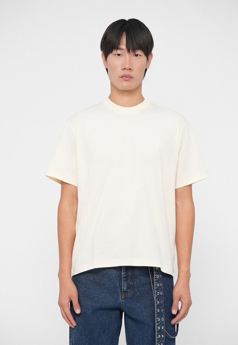 Camiseta de manga corta en color crema claro, con cuello redondo, hecha de una tela suave, con un corte relajado y un diseño minimalista.