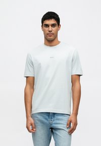 Světlomodré tričko s krátkým rukávem a kulatým výstřihem, s malým logem "BOSS" na hrudi. Nošeno s světlomodrými džínami.