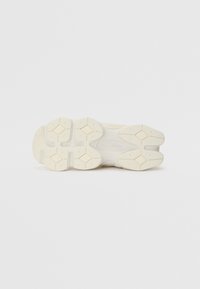 Semelle de sneaker blanche avec un design en caoutchouc texturé présentant des motifs en forme de diamant et des crêtes pour l'adhérence. La marque est visible sur la semelle.