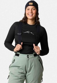 Black long-sleeve top with mountain logo, paired with light green snow pants, featuring adjustable straps and zippered pockets.