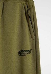 Oliwkowe spodnie dresowe z elastycznym pasem, kieszenią boczną i czarnym nadrukiem logo z czaszką oraz napisem "Diverse ExtremeTeam.com."