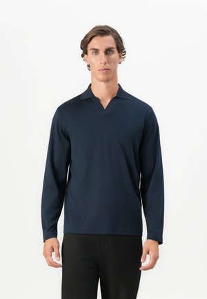 Polo de manga larga azul marino con cuello en V y una textura suave. Diseñado para un ajuste ceñido, combinado con pantalones negros.